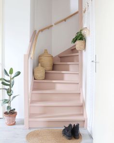 some shoes are sitting on the floor in front of a pink stair case and potted plant