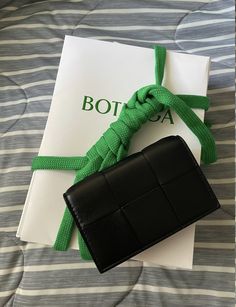 a black wallet with a green ribbon tied around it sitting on top of a bed