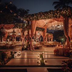 an outdoor wedding venue decorated with flowers and lights at night time, surrounded by greenery