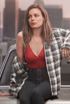 a woman sitting on the hood of a car in front of a cityscape