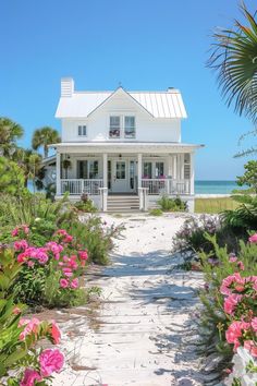 a white house with pink flowers in front of it and the ocean in the background