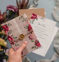 a person holding two wedding cards with flowers on them and a wax seal in the middle