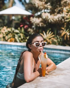 a woman sitting next to a swimming pool with a drink in her hand