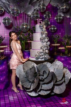 a woman standing next to a tall cake on top of a purple tablecloth covered floor