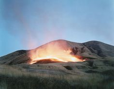 a large volcano spewing out lava into the air on top of a grass covered hill