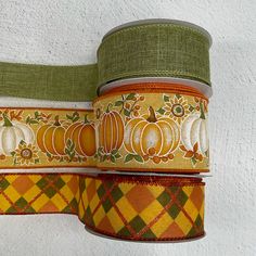 three rolls of pumpkins and plaid ribbon on a white wall with green trimming