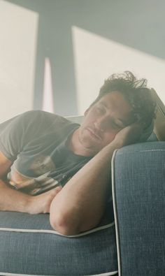 a man laying on top of a blue couch next to a white and gray wall