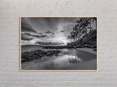 a black and white photo hanging on a brick wall next to the ocean with palm trees