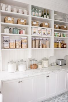 a kitchen with white cabinets and shelves filled with food