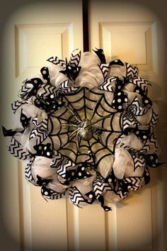 a spider web wreath hanging on the front door with black and white ribbons around it