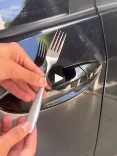 a person is holding a fork and knife in front of a car door handle that has been pulled open