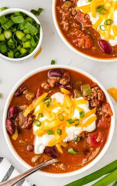 two bowls filled with chili, beans and sour cream on top of a white table