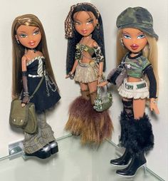 three dolls are standing next to each other on a glass shelf in front of a white wall