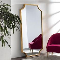 a large mirror sitting next to a red chair in a room with a potted plant