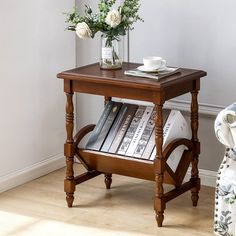 a small wooden table with books on it and flowers in a vase next to it