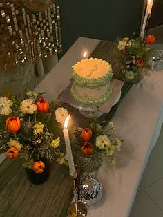 a table topped with a cake and two lit candles next to vases filled with flowers