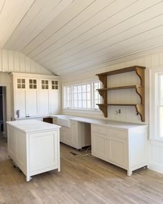 an empty kitchen with white cabinets and wood flooring on the walls, along with open shelving units