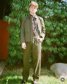 a young man wearing a suit and tie standing in front of a tree with his hands in his pockets