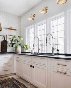 a white kitchen with black counter tops and gold pulls on the faucets above the sink