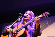 a woman with purple hair is playing the guitar and singing into a microphone on stage