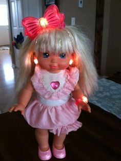 a doll with blonde hair wearing pink shoes and lights in her hair is standing on a wooden floor