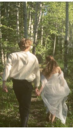 a man and woman are walking through the woods holding hands, both dressed in white