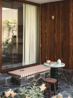 a table and two stools in front of a window with wood paneled walls