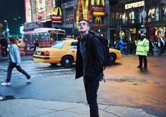 a man standing on the side of a street next to a yellow taxi and people