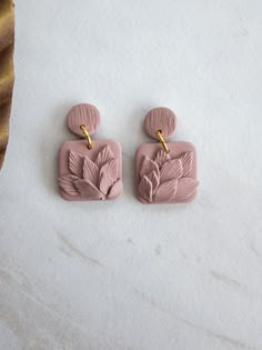 two pink earrings with leaves on them sitting on a white table next to a gold tie