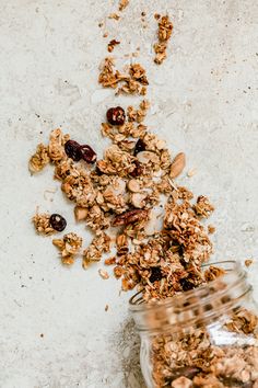 granola in a glass jar next to a pile of nuts and cranberries