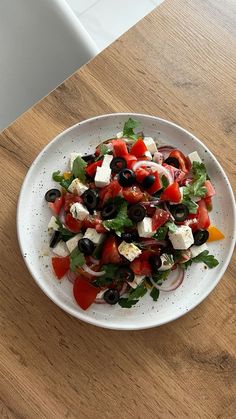 a salad with tomatoes, olives and feta cheese in a white bowl on a wooden table