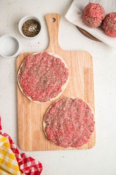 two hamburger patties sitting on top of a cutting board next to a bowl of seasoning