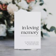 a white card with the words in loving memory on it next to flowers and greenery