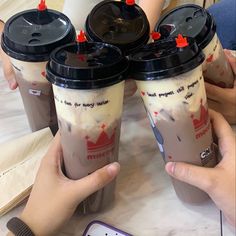 three people holding up two cups of coffee with red caps on their lids and one is holding a cell phone