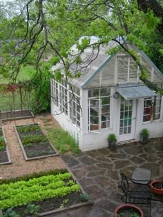 a small white house sitting in the middle of a yard with lots of green plants