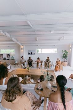 several people sitting at tables in a large room with white walls and ceilings, talking to each other