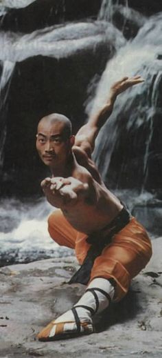 a man in orange shorts is doing a trick on a rock with waterfall behind him