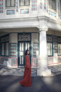 a woman standing in front of a building with green shutters and red dress on