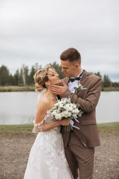 a bride and groom standing next to each other in front of a body of water