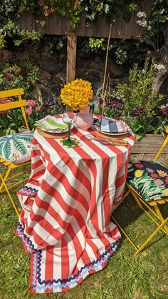 an outdoor table set up with flowers and plates on it, next to a wooden fence