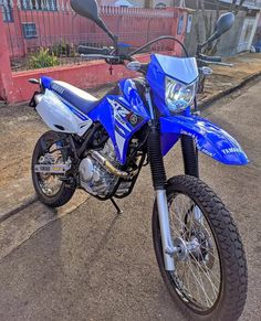 a blue dirt bike parked on the side of the road in front of a red building