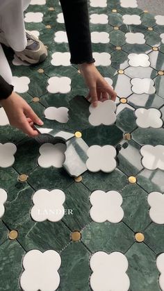 a person cutting up some white and gold circles on a green marble floor with scissors