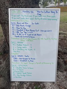 a white board with writing on it next to a tree