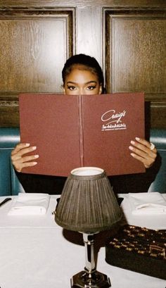 a woman sitting at a table with a book in front of her face while holding it up