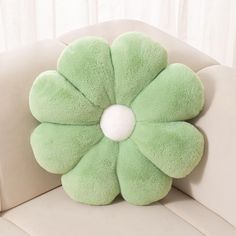 a green flower shaped pillow sitting on top of a white couch next to a window