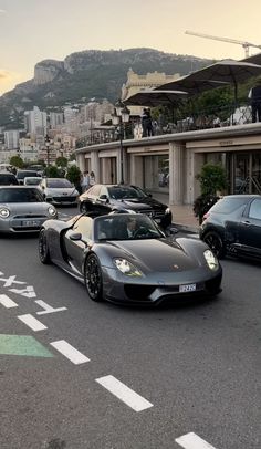 a group of cars driving down a street next to a tall building with a mountain in the background