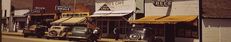 several old cars parked on the side of a road in front of buildings with awnings