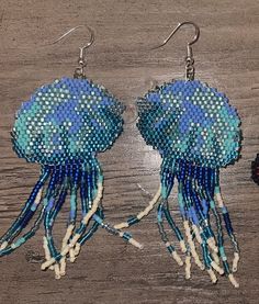 two blue and white jellyfish earrings are on a wooden table next to each other