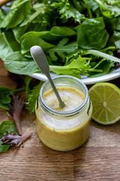 a glass jar filled with dressing next to a pile of lettuce and lemon wedges