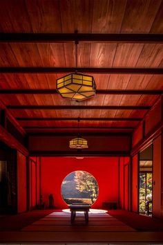 an empty room with red walls and wood ceilinging is lit by a round light fixture